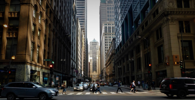 People use a crosswalk to cross a road between skyscrapers.