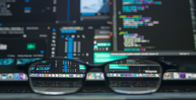 A pair of glasses lie on a laptop keyboard, in front of a page full of code.