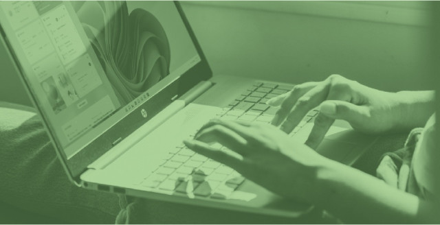 A person sits in a window seat while working on a laptop computer, overlaid with a color filter in Duo green